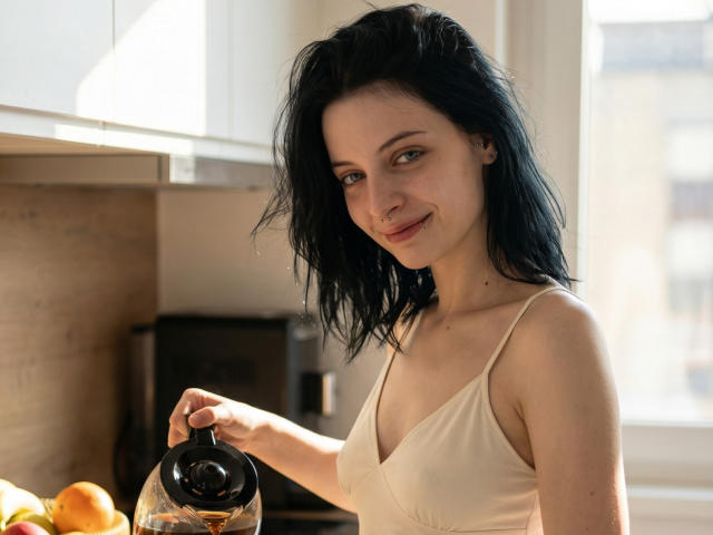 Photograph of MelyndaMarron, a pale-skinned woman with black hair, wearing a beige tank top, holding a glass pitcher, sunlight streaming in, subtle smile, bright kitchen, orange fruit in foreground.