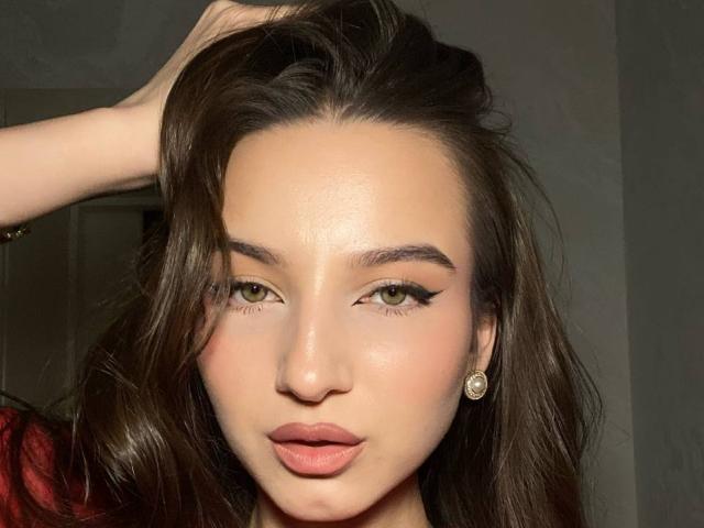 Primo piano di MargertLewi, con lunghi capelli scuri, una mano tra i capelli, un'espressione sensuale, labbra piene, pelle chiara, occhi verdi, con un trucco che accentua lo sguardo. eyeliner, piccoli orecchini di diamanti, illuminazione ad alto contrasto, sguardo intenso, sexy.