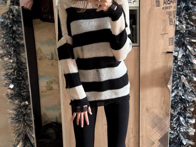 Photograph of DelfinaAuble wearing a black-and-white striped knit sweater, black fingerless gloves, and black pants. She's standing in front of a wooden door with black tinsel on both sides. Fucking hot.