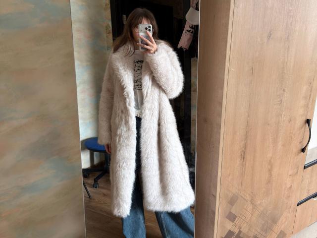 Selfie allo specchio di DelfinaAuble, in piedi in una stanza, che indossa un cappotto bianco soffice, jeans blu e tiene in mano un telefono. custodia decorata, che si riflette in uno specchio di legno. Molto attraente..