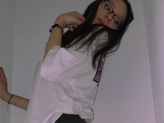 RavenBlisss, avec ses longs cheveux noirs, ses lunettes et sa chemise blanche, pose, une main près de son visage, l'autre main tendue. cadre.
elle a un bracelet à son poignet. Putain, elle est sexy..