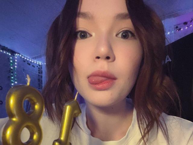 Close-up photo of FarahCantre with slightly parted lips, brown wavy hair, and pale skin. Gold "8" and "1" candles in foreground. Blurred string lights in background. Fucking birthday vibe.