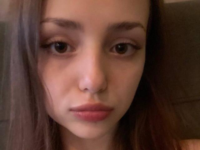 Close-up foto van TrevaGiumarro met donkerbruine ogen, volle lippen en recht bruin haar dat gedeeltelijk het linkergedeelte bedekt. kant. Zacht licht, serieuze uitdrukking, subtiele schaduw op de rechterwang..