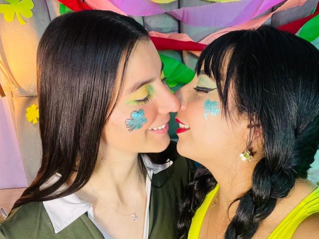 Due donne con i capelli scuri, una di fronte all'altra, con i nasi quasi a contatto. Entrambe hanno brillantini blu sulle guance e ombretto verde. Una indossa una maglietta verde, l'altra una gialla. Tensione intima, sensuale e sessuale..