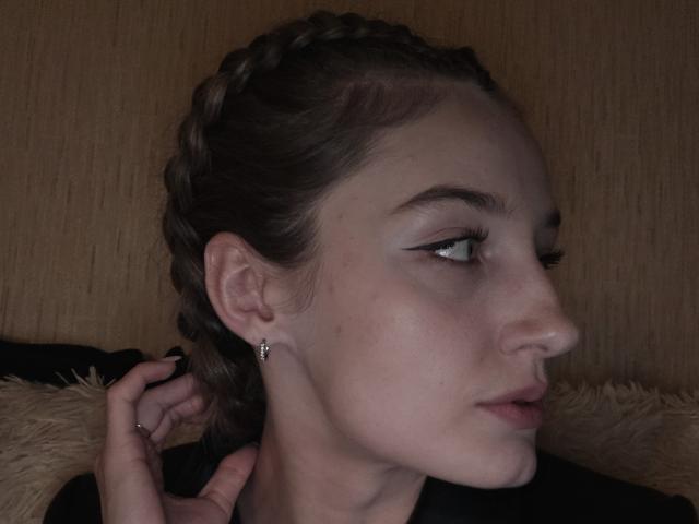 Close-up van het profiel van DiedraBloschichak, donkerbruin gevlochten haar, bleke huid, dikke zwarte eyeliner, kleine oorringen. Naar rechts kijkend, hand die haar nek aanraakt, gedimd licht, sensuele uitdrukking..