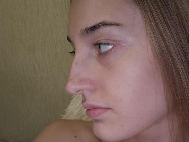 Close-up of DiedraBloschichak's profile, showing her light skin, blue eyes, and subtle smile. Her brown hair is tucked behind her ear. She has a slight sheen on her face. Fucking gorgeous.