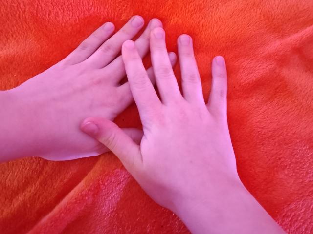 Two pale hands rest on a bright red, textured towel. Fingers slightly intertwined, soft pinkish skin contrasted against vibrant red. Foreground focus, hands centered, towel's texture visible.