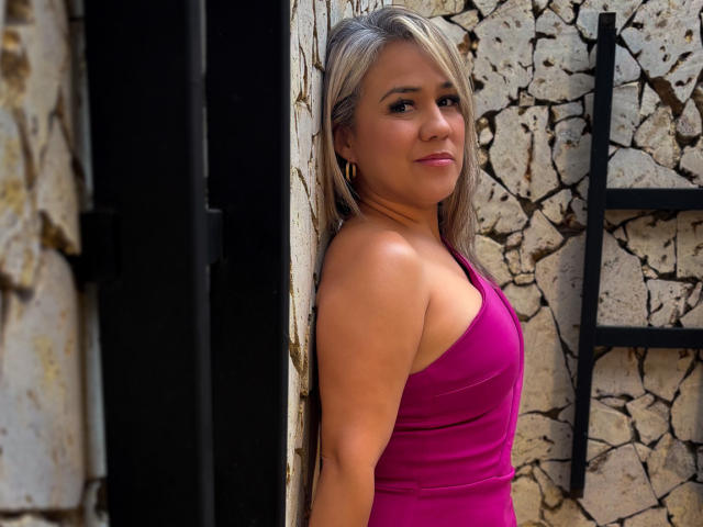 Foto van CamilaNoer die leunt tegen een gebarsten stenen muur, gekleed in een strak roze tanktop, met lang blond haar, en een serieuze uitdrukking. uitdrukking, subtiele glimlach, natuurlijk licht, buitenlocatie, nonchalante pose, aantrekkelijk.