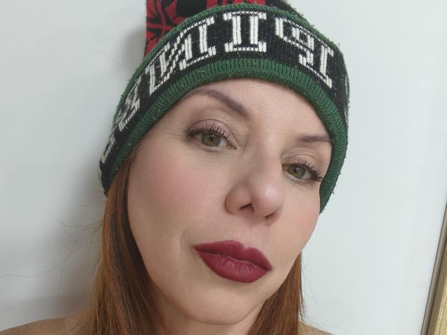 Primo piano di Khharha, con la pelle chiara, i capelli castani e il rossetto rosso. Indossa un berretto verde con la scritta bianca "NORTHFACE". Trucco leggermente sbavato, espressione neutra, leggero rossore sulle guance. Assolutamente attraente..