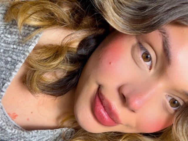 Close-up foto van EmmaRiveraa, lichtbruin krullend haar, roze blush op de wangen, bruine ogen, draagt een glinsterende grijze top. lichte glimlach, lippen lichtjes open, seksuele spanning, intieme blik, zachte verlichting.