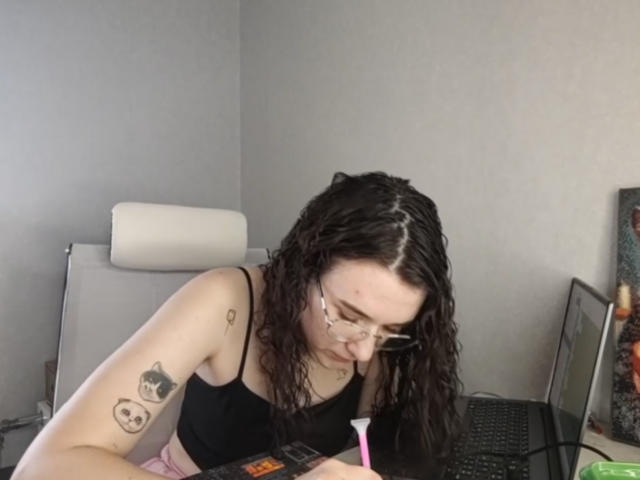 Natosha Burdine, una mujer de piel clara con cabello negro largo y rizado, se inclina sobre una computadora portátil, usando gafas y una blusa negra. mostrando un tatuaje de una "cara sonriente" en su brazo. Concentrado, sexy, solo..
