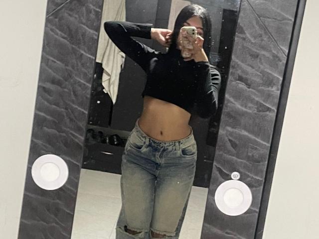 JanneClowses, selfie allo specchio, indossa un top corto nero, che lascia scoperto il ventre, jeans strappati, una mano dietro la testa, telefono davanti. viso, sfondo scuro, icone di iPhone sullo specchio, casual, sexy, posa sicura..