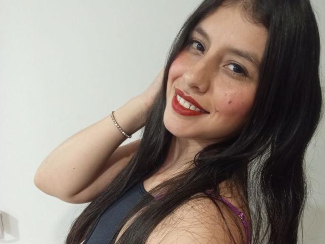 MadissonFontaine has long black hair, fair skin, red lipstick, and a slight smile. She's wearing a black tank top, with her hand raised behind her head. Fucking cute, sexy, and confident.