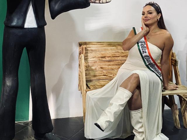 GalaMalkova, assise sur un banc en bois, portant une robe blanche avec une ceinture noire et blanche, des bottes blanches, est penchée en arrière. Avec une jambe levée, regardant un homme debout. Tension sexuelle.