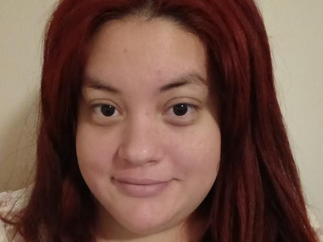 Gros plan de LalaQueen, une jeune femme aux longs cheveux bruns lisses, à la peau claire et au sourire discret. Ses yeux marrons regardent directement l'appareil photo. Son expression est détendue..