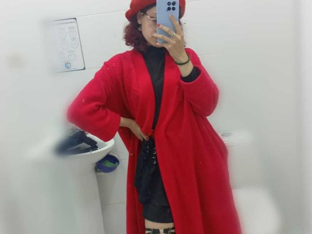 SophieBlake in a bathroom selfie, wearing a red robe, black top, and thigh strap, holding a phone, red hat, hand on hip, cock visible under robe, mirror reflection.