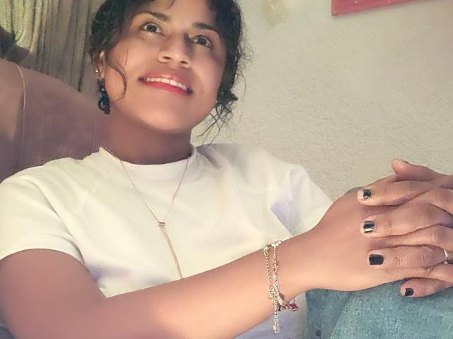 Foto van Ivanna Duran met een bruine huid en donker krullend haar, die lacht met rode lippen. Ze draagt een wit T-shirt, zwarte nagellak en een zilveren armband, met haar handen samengevouwen. Duidelijke seksuele spanning..