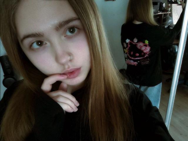 TerraMaul has light skin, long brown hair, and a nose ring. She's biting her finger with a sultry expression. Wearing a black shirt, reflected in a mirror. Fucking sexy.