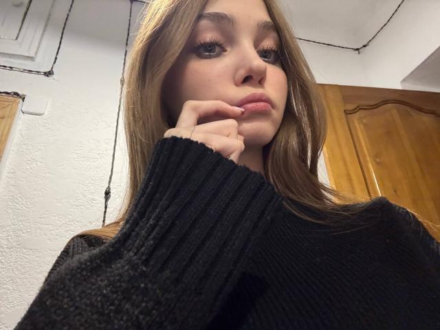 Primer plano de Calista Swiatek, morena con cabello largo, vestida con un suéter de punto negro, con la mano tocándose la barbilla, con una expresión seductora. mirada, puerta de madera y pared blanca en el fondo, iluminación suave, rostro ligeramente en sombra..