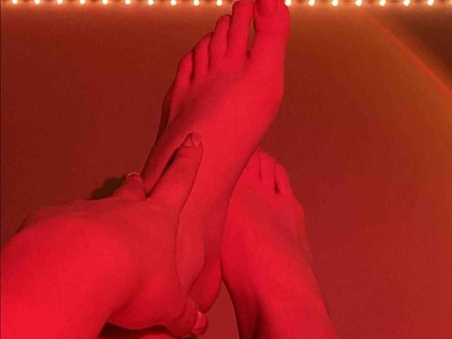 Fotografía con iluminación roja de los pies cruzados de SarahyJhones, con los dedos de un pie tocando el tobillo del otro, y una guirnalda de luces blancas. gastos generales.
su muñeca izquierda lleva una pulsera de plata. Una vibra erótica, la verdad..