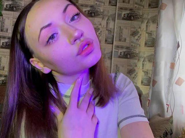 RonnieWeeda, close-up, facing camera, purple-blue lighting, dark brown hair, heavy makeup, slightly open mouth, hand touching neck, white shirt, newspaper pattern background, seductive expression, soft focus, casual pose.