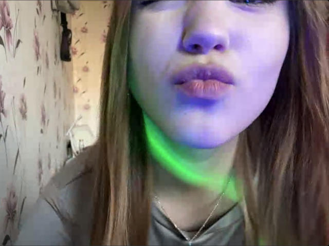 Primo piano di CorinaMakinster con la pelle di colore bluastro, una luce verde sul collo e i capelli castani. Ha labbra piene, leggermente dischiuse. Indossa una camicia grigia, con un leggero ombretto sul viso..