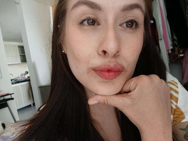 Nahaufnahme von Isabella Palacio, einer brauen Frau mit langen, dunklen Haaren, rotem Lippenstift und heller Haut, die ihr Kinn auf ihre hand, die einen leichten Schmollmund zeigt, Innenraum, Küchenhintergrund. Verdammt heiß..