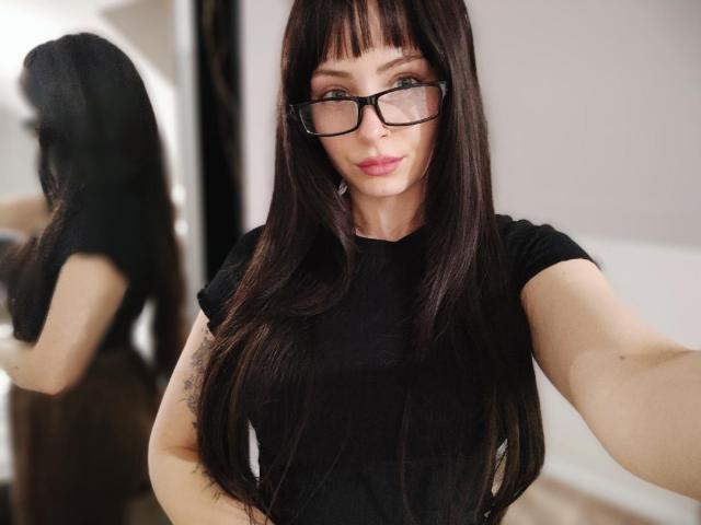 NoemiLou, avec ses longs cheveux noirs et ses lunettes à monture noire, prend un autoportrait. Elle porte une chemise noire, qui laisse entrevoir sa aisselle. Le reflet dans le miroir montre son dos. Un look incroyablement séduisant et plein d'assurance..