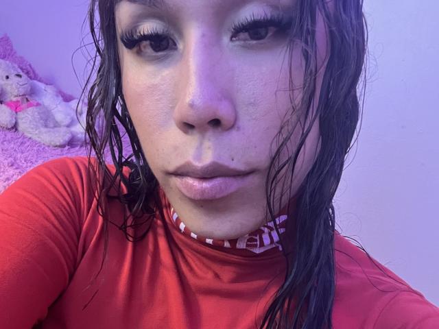 Gros plan de GeraldineSuan, les cheveux mouillés, portant une chemise rouge, regardant directement l'appareil photo avec les yeux à moitié fermés. gloss à lèvres discret, léger sourire, éclairage bleu doux, jouet en peluche en arrière-plan.