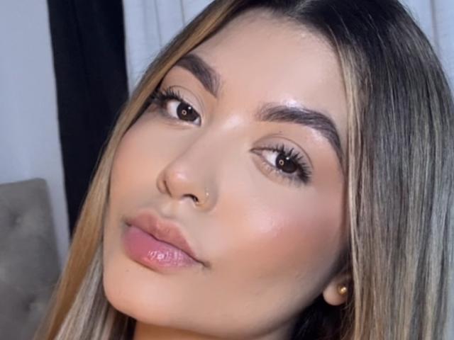 Close-up foto van LauMiller, een jonge vrouw met lang, steil bruin haar, lichte huid en een neusring. Ze heeft volle lippen, glanzende roze lippenstift en goed gedefinieerde wenkbrauwen. Heel aantrekkelijke uitstraling.