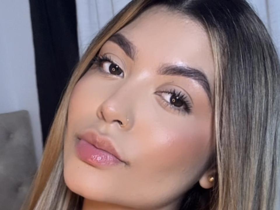 Close-up photo of LauMiller, a young woman with long, straight brown hair, fair skin, and a nose piercing. She has full lips, glossy pink lipstick, and well-defined eyebrows. Fucking sexy look.