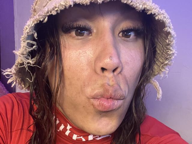 Close-up of GeraldineSuan with puffy lips, wearing a frayed straw hat and red shirt. Her face is slightly flushed, with visible acne and dark, wet hair. Fucking intense expression.