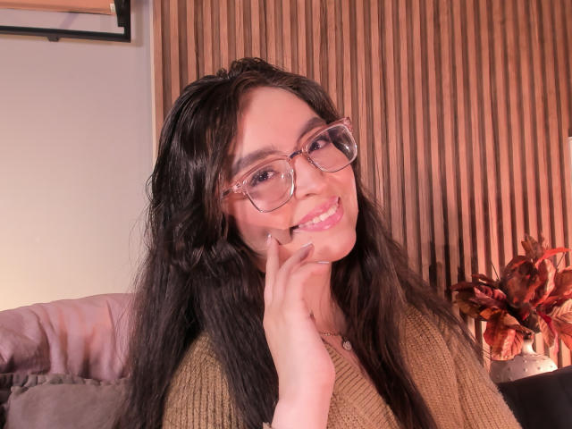 EvaMcAllister, mulher asiática com cabelos longos e pretos, usando óculos e um suéter marrom, mordendo o dedo, sorrindo. de forma sedutora.
fundo de painel de madeira, planta vermelha no canto, iluminação suave. Incrivelmente atraente..