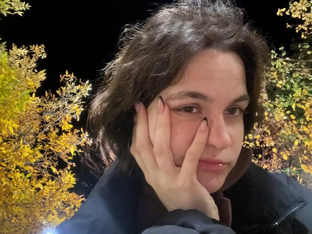 Fotografia di LahomaLoven, una giovane donna con capelli scuri di media lunghezza, che si tocca il viso con una mano, vestita di nero giacca.
foglie autunnali con sfumature gialle e arancioni sullo sfondo. Espressione assolutamente meravigliosa..