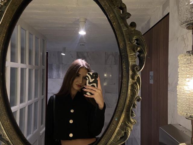 El reflejo en un espejo ovalado ornamentado muestra a BiancaMassimo con cabello largo y oscuro, una blusa negra abotonada, sosteniendo un teléfono con patrón en blanco y negro.
lámpara colgante, paredes de mármol, candelabro. Increíblemente atractivo..