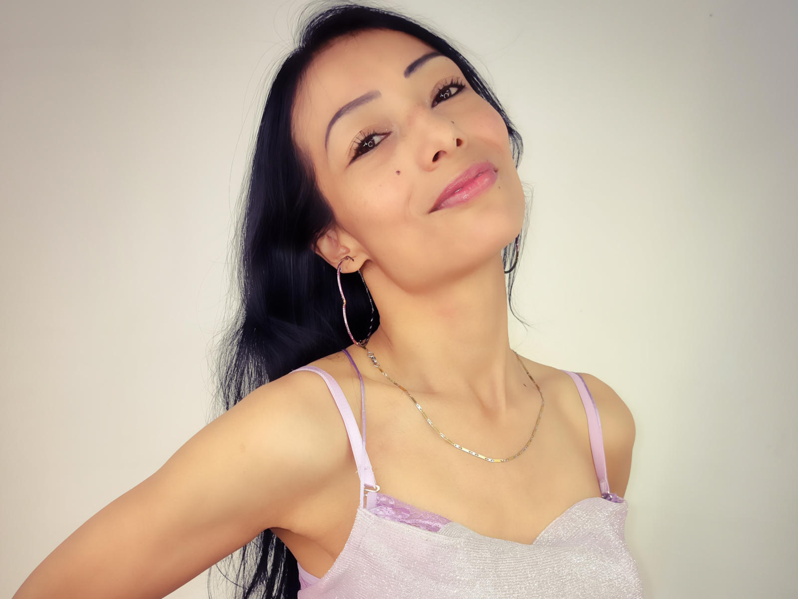 Fotografia de AlejandraCheryy com cabelo preto longo, blusa de renda branca, seios pequenos, pele clara, sorriso discreto, cabeça. inclinada para trás, maquiagem leve, brincos de argola, colar, iluminação suave, leve sombra..