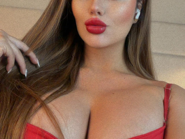 Photo en gros plan de MissAry, mettant l'accent sur son visage et sa poitrine. Elle a de longs cheveux bruns, des lèvres rouges pulpeuses, et porte un soutien-gorge rouge qui met en valeur ses seins volumineux et ronds. Sa main effleure ses cheveux
.