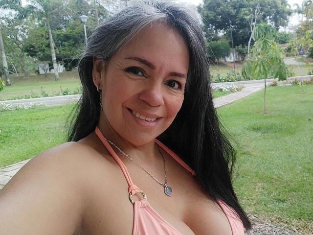 Laila Castillo, avec ses longs cheveux noirs, sourit à l'appareil photo, portant un haut rose à enfiler qui dévoile sa poitrine, et se tient debout. Un parc verdoyant avec des arbres et des chemins en arrière-plan. La lumière du soleil illumine sa peau
.