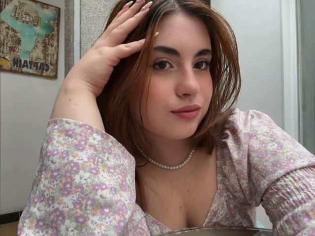 VicluX with light skin, brown hair, and a floral dress, hand in hair, pearl necklace, slight pout, cleavage visible. Background: map of Paris. Casual, sexy, slightly provocative pose.