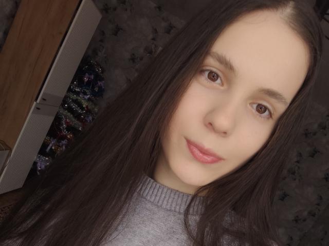 Autoritratto ravvicinato di Olyanash, una donna dalla pelle chiara con lunghi capelli neri, occhi marroni e labbra rosa, che indossa un abito grigio. Maglia a collo alto. Lo sfondo è scuro con sottili motivi a stelle. Estremamente attraente..