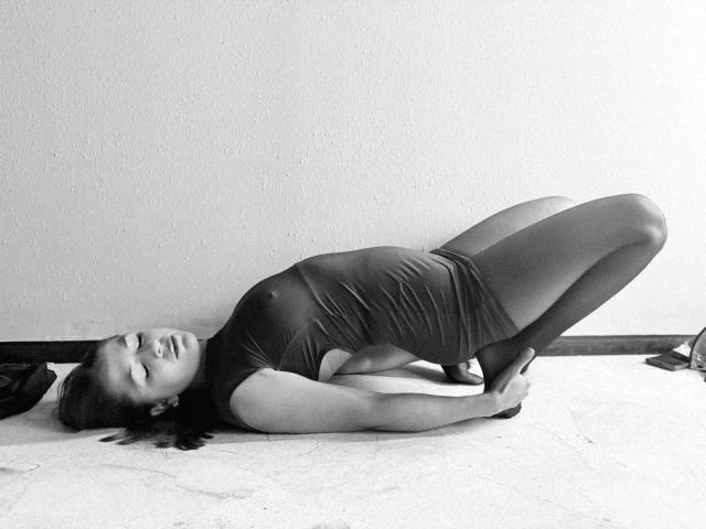 Photo en noir et blanc de MoonXVelvet allongée sur le dos, les jambes pliées au niveau des genoux, portant une combinaison moulante sombre. Les yeux de MoonXVelvet sont fermés, son expression est détendue. Contraste élevé, pose sensuelle..