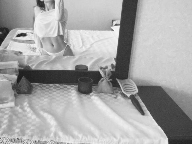 Zwart-wit foto van een badkamer. De reflectie van EmeraldWeinreb in de spiegel toont hun onderrug en billen. Handdoeken en toiletartikelen op de wastafel, kam aan de rechterkant. Er wordt een seksuele spanning gesuggereerd..