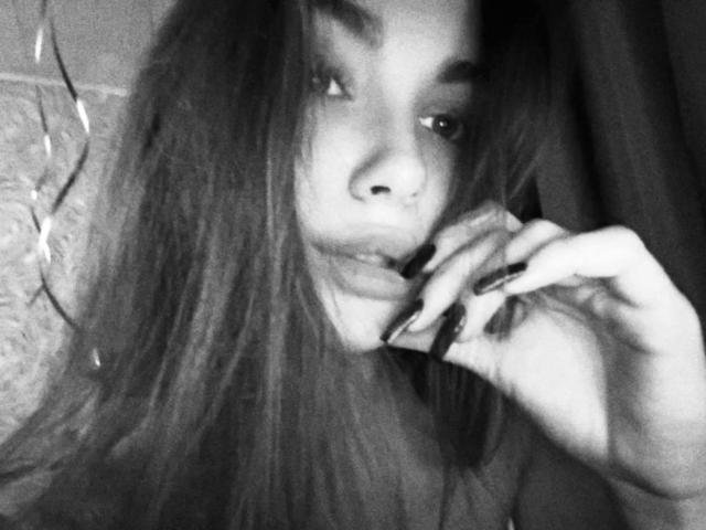 Fotografía en blanco y negro de Emerald Weinreb con el pelo largo, mordiéndose el dedo de forma seductora. Sus ojos están entrecerrados, creando una expresión provocativa y seductora. La imagen tiene un alto contraste y grano..