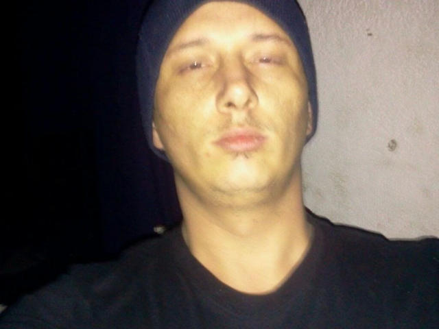 Foto borrosa de maxKnd-hot, que lleva un gorro negro y una camiseta negra, con un rostro ligeramente brillante y rasgos faciales mínimos. características, y un fondo oscuro. Muy atractivo/a, pero la cara está desenfocada..