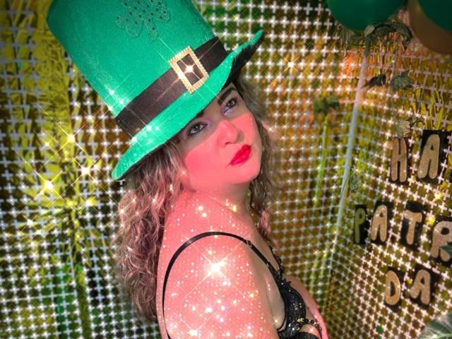 AdrianaPrettie draagt een glinsterende groene hoed met een zwarte band en een zilveren gesp, en kijkt verleidelijk over haar schouder. schouder. Ze heeft krullend haar, rode lippenstift en een huid met glitters. Een heldere, glinsterende achtergrond..