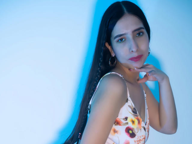 Photograph of IvanaClark, a sexy woman with long black hair, wearing a floral dress, biting her finger, blue light casting a cool glow, intense gaze, subtle sexual tension, slight smirk.