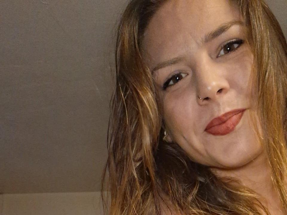 Primo piano di Cocominette, una donna con capelli castano chiaro, leggermente spettinati, che indossa rossetto rosso e guarda la fotocamera. un sorriso appena accennato. L'illuminazione proietta delle ombre delicate sul suo viso. L'attenzione è concentrata sul suo viso, con una palpabile tensione sessuale..