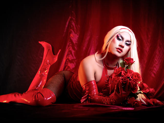 Digital artwork of StefyBratz, a sexy blonde woman with red latex gloves and thigh-high boots, lying on her stomach, holding red roses. Red lighting highlights her seductive pose.
