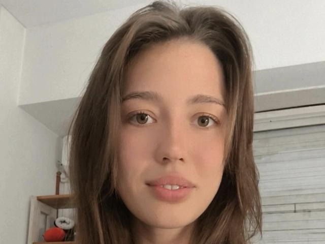 Gros plan de ValeriusBertie, avec des cheveux bruns en bataille, des yeux bruns doux et une peau claire. ValeriusBertie affiche un sourire discret, regardant directement l'appareil photo, avec une fenêtre en arrière-plan..