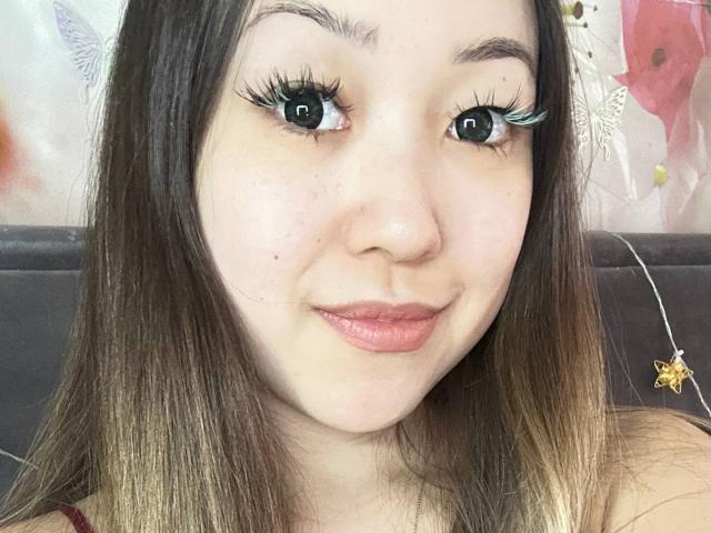 Close-up of RenyLime with fair skin, black hair with blonde tips, and heavy black eyeliner. She's smiling subtly, looking directly at the camera with a hint of sexual tension.